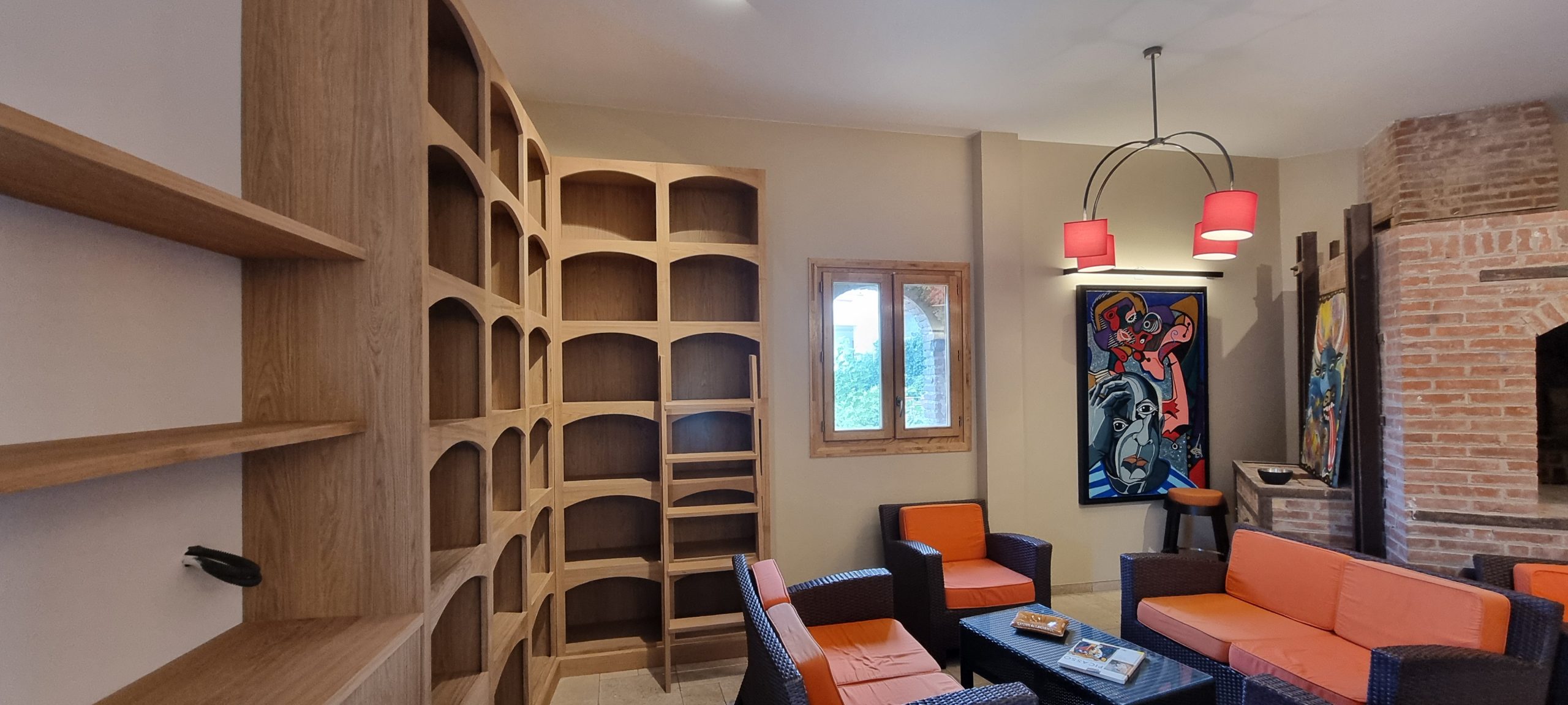 Salon avec bibliothèque en bois à niches arrondies, assises orange et mur en briques