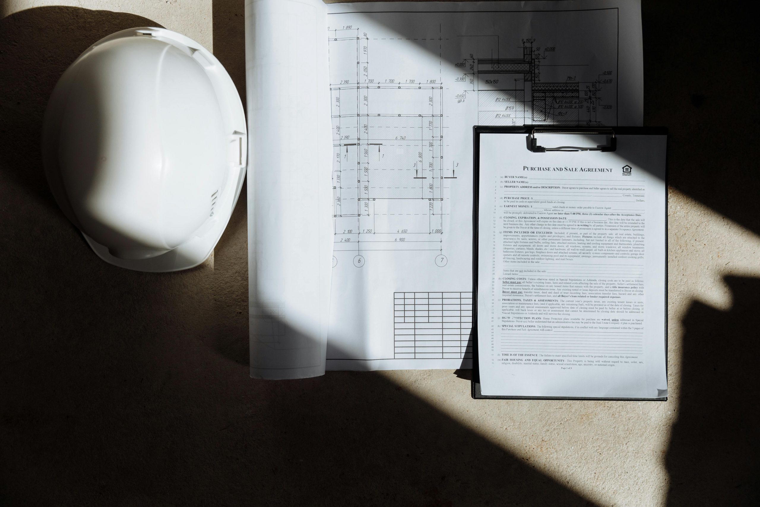 Top view of construction documents and hard hat in sunlight, capturing planning essence.